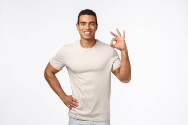 Kendinden emin ve memnun İspanyol bir genç, iyi durumda, tamam gösteriyor, onay ya da iyi işaret veriyor ve anlaşarak gülümsüyor, olumlu geri bildirim yapıyor, ürün öneriyor, beyaz arka plan
