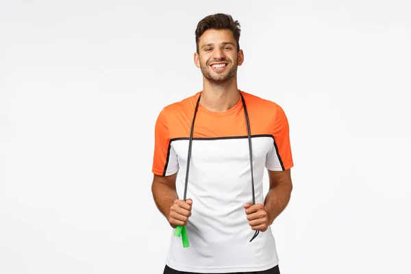 Hombre guapo alegre y saludable en ropa deportiva que sostiene la cuerda de salto alrededor del cuello, sonriendo complacido y entusiasta después del entrenamiento, jogging matutino y ejercicio de resistencia, promueve un estilo de vida activo —  Fotos de Stock