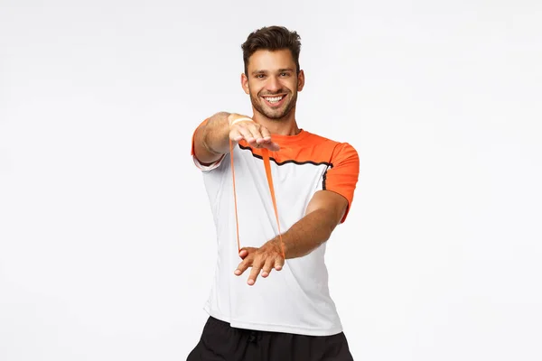 Carismatico istruttore di fitness maschile in activewear mostrando esercizi di fitness, insegnare ai clienti come allenamento con banda di resistenza, stretching con le mani e sorridente, allenamento e concetto di stile di vita attivo — Foto Stock