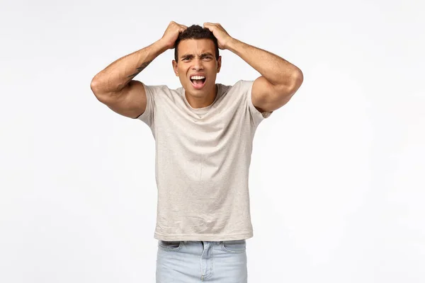 Homem atlético decepcionado em t-shirt, pegue a cabeça e puxe o cabelo incomodado, franzindo a testa chocado e frustrado, perdeu muito dinheiro, se sentir traído ou decepcionado, de pé fundo branco angustiado — Fotografia de Stock