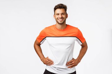 Fitness, spor ve aktif yaşam tarzı konsepti. Stüdyo portresi, spor kıyafetli yakışıklı genç erkek antrenör, kollarını belinden tut, arkadaşça gülümse ve kararlı ol, kafanı oyuna ver, çalışmaya hazır ol.