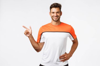 Erkeksi, beyaz sakallı, formunda bir adam, spor eğitmeni müşterilerine talimatlar veriyor, solu gösteriyor ve gülümsüyor, spor salonuna davet ediyor, yeni vücut geliştirme metodu öneriyor.