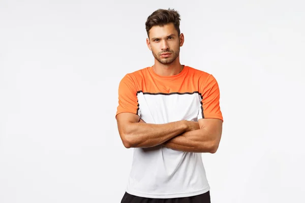 Serious masculine man with bristle, wear sports t-shirt, cross arms over chest, squinting, look camera determined, listening to coach instructions during gym training session, white background — ストック写真