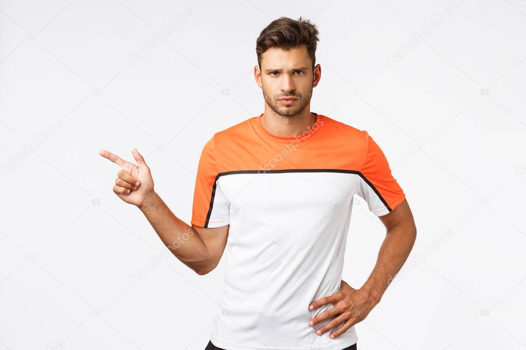 Upset serious-looking sad masculine bearded man in sports, football t-shirt, pointing left frowning disappointed, looking frustrated and questioned what happened, standing offended, white background