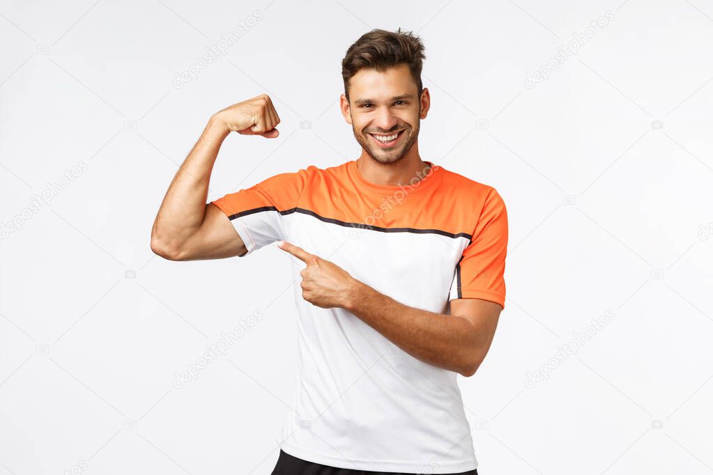 Guy brag with muscles asking if you want touch or gain such good body shape yourself. Sassy smiling, satisfied sportsman show biceps, pointing at arm and grinning, encourage train and workout in gym