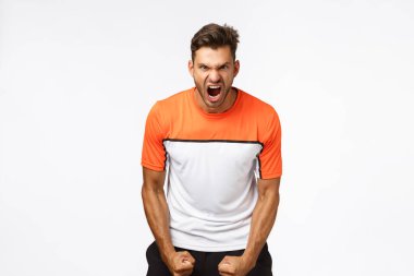Güç, güç ve spor konsepti. Yakışıklı agresif ve güçlü genç sporcu, sıkı yumruklar ve gergin kaslar, takımı daha iyi oynamaya teşvik etmek, kararlı ve iddialı bağırmak, kaslı vücut.
