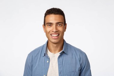 Mavi tişörtlü, neşeli, arkadaş canlısı, bronz tenli genç adam, gülüyor, gülümsüyor coşkulu, neşeli bir ifadeyle kameraya bakıyor gibi, komik ve neşeli bir şey tanıtıyor.