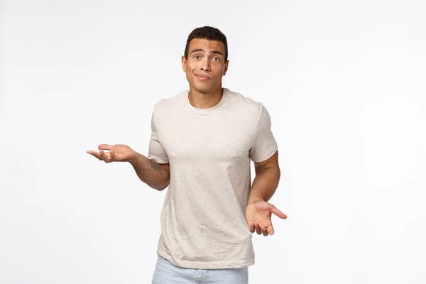 Clueless handsome young hispanic muscular man in casual t-shirt, shrugging, spread arms sideways, smirk and look indecisive, dont know how solve situation, standing puzzled and confused — Stock Photo, Image