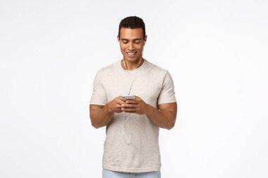 İletişim, teknoloji ve mobil cihaz konsepti. Sıradan kıyafetler içindeki yakışıklı atletik adam, kulaklık takan, akıllı telefonu tutan ve gülümseyen cep telefonu görünümlü ekran, mesaj arkadaşı, metroda video izleyen.