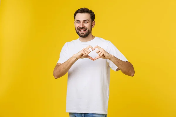 Glimlachende jonge jongen maken hart gebaar op zijn borst met wit shirt geïsoleerd op gele achtergrond — Stockfoto