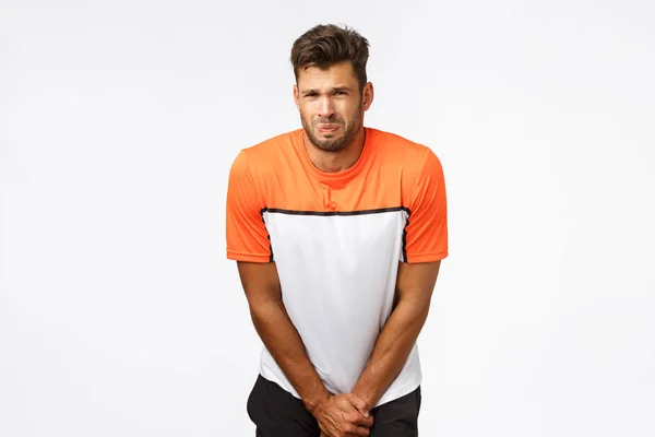 Poor young sportsman, football player in sports t-shirt, bending and grab groin area as feeling pain after player kicked ball, grimacing from painful feelings, squinting, suffering ache — Stock Image Poor young sportsman, football player in sports t-shirt, bending and grab groin area as feeling pain after player kicked ball, grimacing from painful feelings, squinting, suffering ache Royalty Free Stock Images