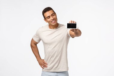 Etkileyici, yakışıklı İspanyol görünümlü, iyi görünümlü, fitness uygulamasını destekleyen, gülümseyen, elini uzatan, akıllı telefon tutan, reklam uygulaması, beyaz arka plan