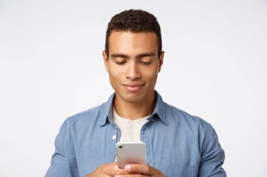 Yakışıklı, modern İspanyol kıyafetli, akıllı telefon tutan, kız arkadaşına mesaj yazarken gülümseyen, sosyal medyayı kaydıran, üniversite dersinde komik videolar izleyen,