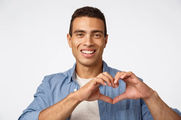 Love, cherity and affection concept. Charming young brazilian masculine man showing heart sign and smiling happy, make surprise dinner for valentines day, arrange christmas romantic night — Stock Photo, Image