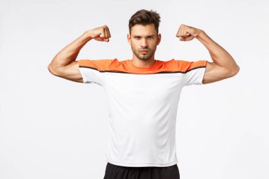 Güçlü, küstah ve yakışıklı genç sporcu, kendine iyi bak, aktif giyin, spor tişörtü giy, kaslarını göster, ellerini kaldır ve kaslı görün, kararlı ve erkeksi görün.