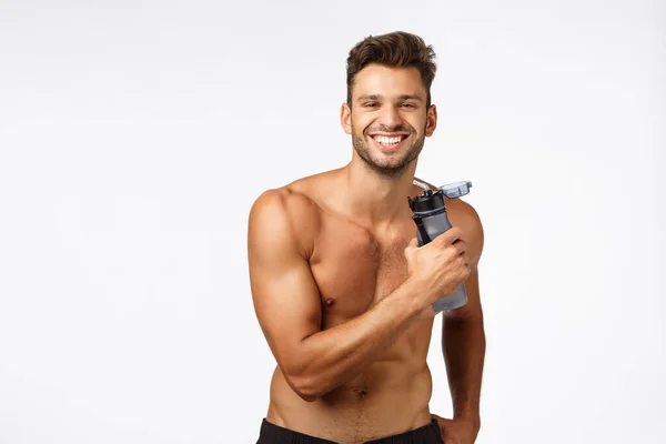 Musclé sexy et insouciant, sportif souriant heureux debout torse nu, tenant bouteille d'eau et sourire ravi, heureux après l'entraînement productif, montrant abdos abdominaux, six-paquets — Photo