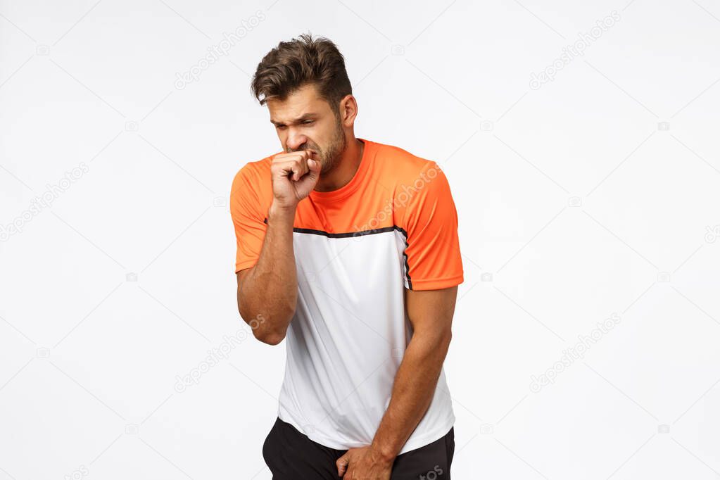 Football player feeling pain, trying hold scream, biting fist and squinting, grimacing as bending and holding arm on groan area, was kicked with soccer ball, endure pain on field, white background