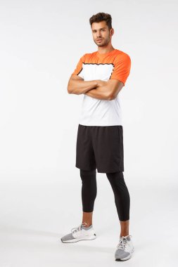 Güven, spor ve fitness konsepti. Dikey çekim iyi görünümlü sakallı yakışıklı spor elbiseli, göğsünde çapraz kollar, kararlı ve ciddi görünüyor, maç kazanmaya hazır.