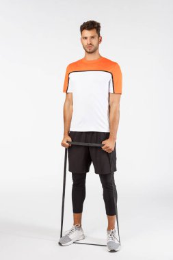 Dikey çekim yakışıklı sakallı genç erkek sporcu spor giyim antrenmanı sırasında futbol oyuncusu antrenmanı, ilmek bantları, ayaklı ve elli esnek direniş ipleri, kararlı görünüyor.