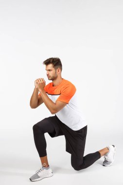 Dayanıklılık, egzersiz ve spor konsepti. Motive olmuş, ciddi görünümlü, aktif giyimli sporcu, dizlerinin üzerine çök, kollarını sıkarak gerginlik yarat, odaklanmış görün, beyaz arka plan üzerinde çalış, tam boy