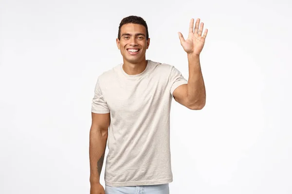 Amistoso hombre atlético alegre en camiseta, levantando una mano y saludando en hola, hola, gesto de saludo, sonriendo encantado y optimista, ver amigo conocer a alguien, de pie fondo blanco alegre — Foto de Stock