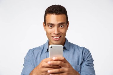 Heyecanlı, şaşkın adam video kaydediyor, müthiş ve heyecan verici bir şey çekiyor, akıllı telefonu tut, patlak gözlerle ekrana bak ve büyüleyici bir gülümsemeyle beyaz bir arka plan yakalamaya çalış.