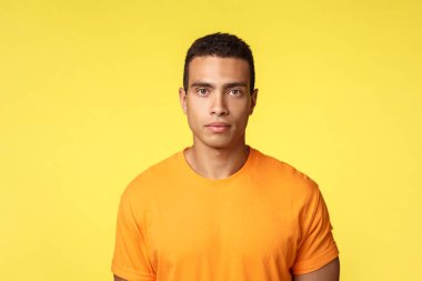 Motivasyon, yaşam tarzı ve spor anlayışı. Ciddi görünüşlü, kararlı, tişörtlü, yakışıklı ve erkeksi bir adam. Kamera, yüz ifadesi yok. Dinleme öğretmeni, sarı arka plan.