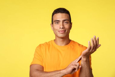 Sağlık, tıp ve yaşam tarzı konsepti. Sarı tişörtlü yakışıklı ve kendinden emin bir adam, nabzını ölçüyor, bir kolunu kaldırıp damarına dokunuyor, sırıtıyor, sporcu kan basıncını ölçüyor.