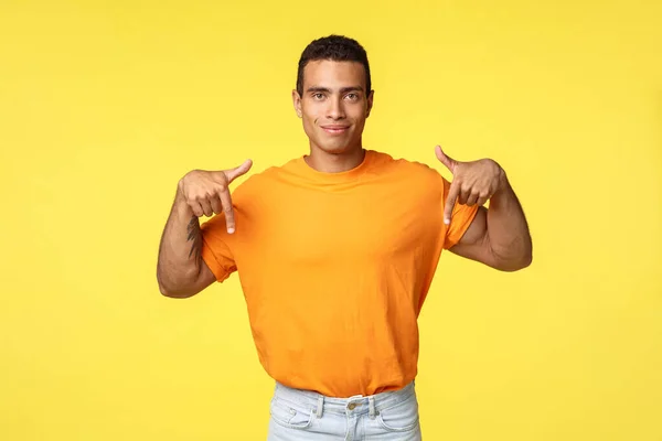 Confident good-looking guy with assertive smile, pointing fingers down to promote banner, smiling as showing good deal, advertise offer, give advice or recommendation, standing yellow background — Stock Photo, Image