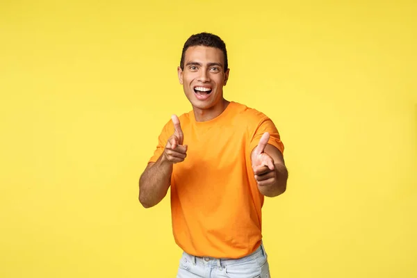 Aufgeregter, freundlicher und kontaktfreudiger junger Mann in orangefarbenem T-Shirt, der mit dem Finger auf die Kamera zeigt, um Sie zu loben, dem Mitarbeiter zu seiner Bewerbung gratuliert, optimistisch lächelt, gelber Hintergrund — Stockfoto