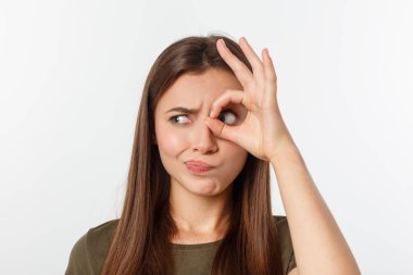 Neşeli, şirin, şık, çekici, trend bir kızın, parmaklarıyla dürbün yapan, gri arka planda izole edilmiş, keyifli bir kız portresi.