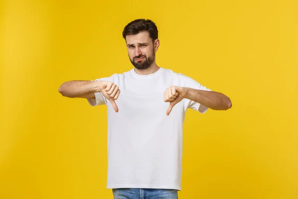 Ung stilig man bär vit t-shirt över isolerad bakgrund Göra tummen ner, oenighet och överens uttryck. Galen konflikt. — Stockfoto
