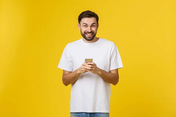 Хорошие новости от друга. Уверенный молодой красивый мужчина в джинсовой рубашке держит смартфон на желтом фоне — стоковое фото