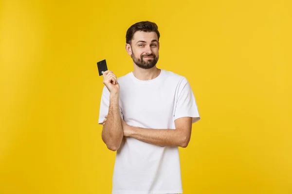 Szczęśliwy uśmiechnięty młody człowiek pokazując kartę kredytową izolowane na żółtym tle — Zdjęcie stockowe