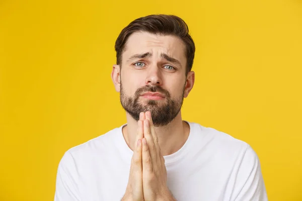 Young guy dressed casually isolated on yellow background, having put hands together in prayer or meditation, looking relaxed and calm.