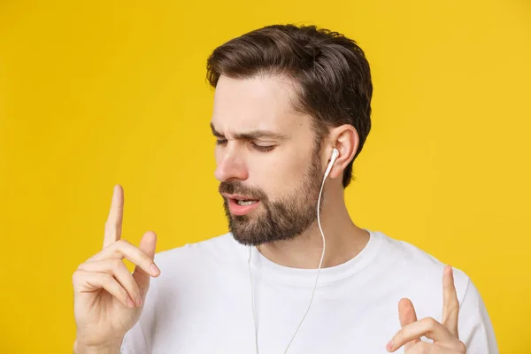 Gut aussehend wie ein junger Mann, der Musik vor gelbem Hintergrund genießt. — Stockfoto