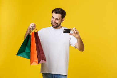 Sarı arka planda izole edilmiş alışveriş torbaları ve kredi kartı taşıyan gülümseyen çiftin portresi..