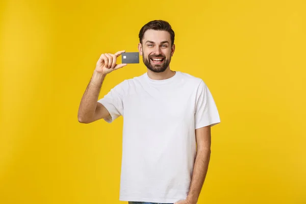 노란 배경에 고립된 신용 카드를 보여 주는 행복 한 미소를 짓고 있는 젊은 남자 — 스톡 사진