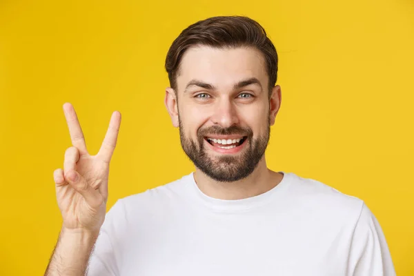 Молодой красивый мужчина в полосатой футболке на изолированном желтом фоне улыбается, глядя в камеру, показывая пальцы, делающие знак победы. Номер два: — стоковое фото