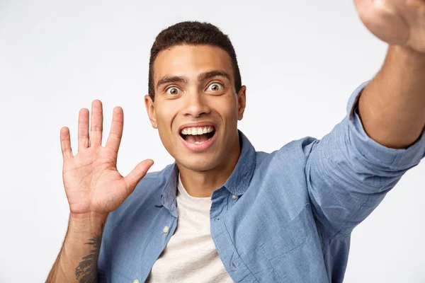 Surpreso e impressionado homem não expact ver alguém como segurando câmera, acenando a mão em Olá ou oi gesto, olhos pop fascinado, boca aberta e sorrindo fascinado, fundo branco espantado — Fotografia de Stock