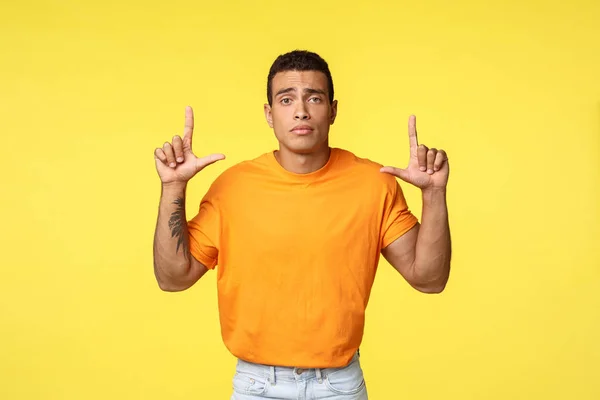 Triste joven caucásico sombrío en camiseta naranja frunciendo el ceño molesto, señalando ofendido o angustiado, perdiendo la competencia, sintiendo tristeza y depresión, de pie frustrado sobre el fondo amarillo — Foto de Stock