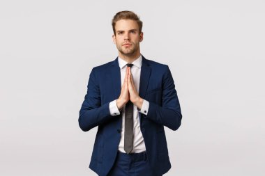 Klasik takım elbiseli kararlı ve kendinden emin genç iş adamı, sarışın sakallı adam, avuç içlerini birbirine bastırıyor ve ileriye bakıyor, meditasyon yapıyor, düşünceli duruyor, dua ediyor, dileğinin gerçekleşmesini bekliyor.
