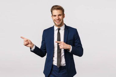Şık ve kendinden emin, klasik mavi takım elbiseli yakışıklı sarışın sakallı adam, solu işaret ediyor, iş ortağı mekanını gösteriyor, toplantı yeri, içeri gel, beyaz arka planda dur.