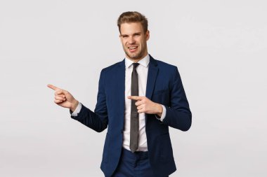 İğrençsin. Hoşnutsuz iş adamı tiksinti duyuyor, uygunsuz, iğrenç bir şey görüyor, solu işaret ediyor, yüzünü buruşturuyor, rahatsız ediyor ve tatmin olmuyor, beyaz arka planda duruyor.