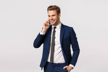 Çekici, başarılı ve varlıklı takım elbiseli beyaz iş adamı, telefonla konuşuyor, akıllı telefonu kulağına yakın tutuyor, yabancı iş ortaklarını arıyor, şirket çalışanlarını tartışıyor, beyaz bir geçmişi var.