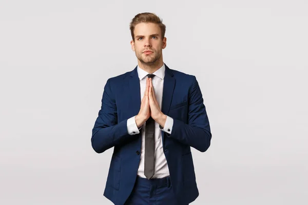 Determined and confident young businessman in classic suit, blond bearded guy, press palms together and looking forward, meditating, standing thoughtful, praying, anticipate wish come true