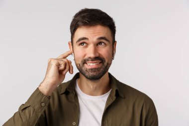 Kaygısız gülümseyen, yakışıklı, sakallı yetişkin erkek, rüya gibi ve neşeli, kablosuz kulaklığa dokunuyor, sesi değiştiriyor ya da bitiriyor, beyaz arka planda mutlu duruyor.