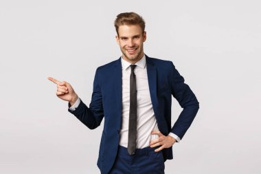 Tüylü iddialı sarışın iş adamı, klasik takım elbise giyiyor, sol ve gülümseyen kamerayı işaret ediyor, harika ürünlerden bahsediyor, reklam uygulaması, iş konsepti, beyaz arka plan