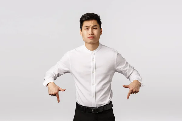 Escéptico arrogante asiático hombre de negocios en camisa blanca, pantalones, apuntando hacia abajo mirar cámara insatisfecho y sin impresionar, enfurruñando, mueca descuidado, expresar aversión o desprecio, fondo blanco — Foto de Stock