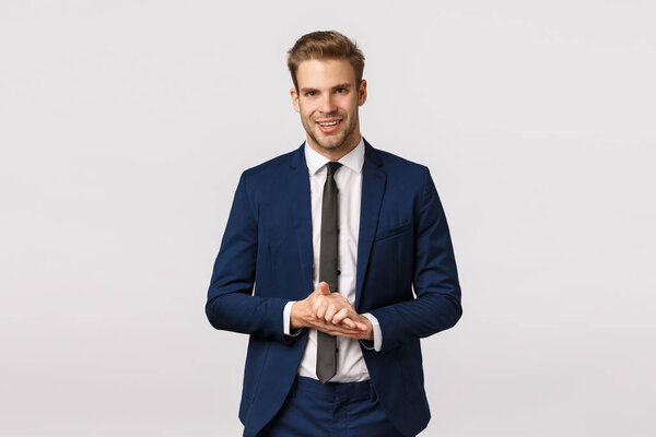 Handsome and confident, smart male entrepreneur in classic suit, rubbing palms and smiling pleased, anticipate make big money, good deal, relish something good, standing white background